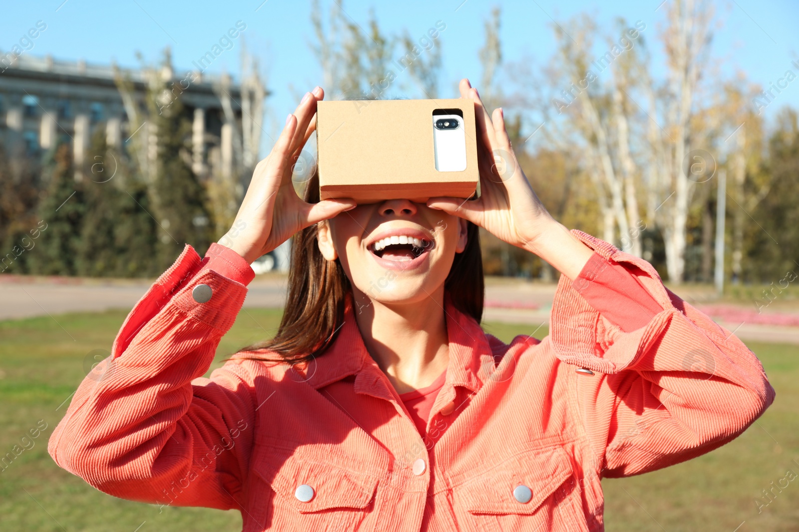 Photo of Young woman using cardboard virtual reality headset outdoors