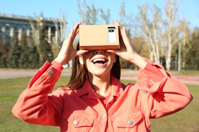 Photo of Young woman using cardboard virtual reality headset outdoors