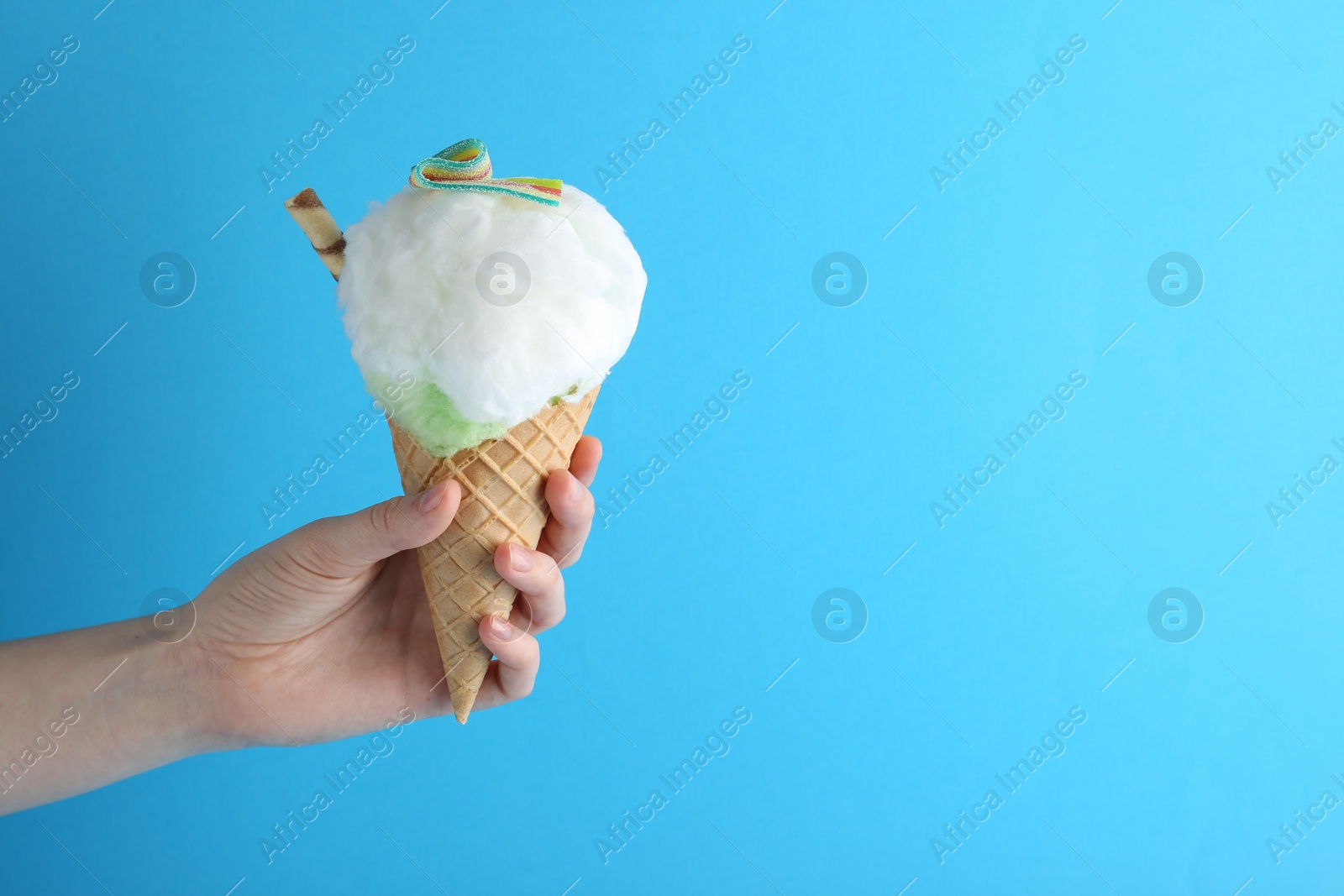 Photo of Woman holding waffle cone with cotton candy on light blue background, closeup. Space for text