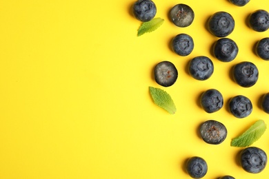 Tasty ripe blueberries and leaves on yellow background, flat lay with space for text