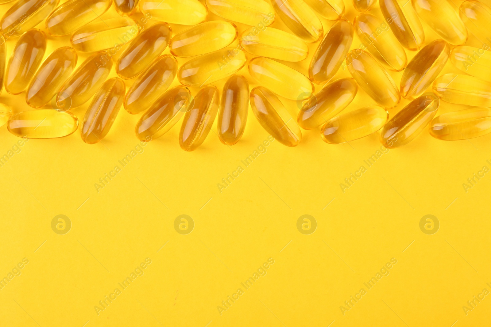 Photo of Many vitamin capsules on yellow background, top view. Space for text