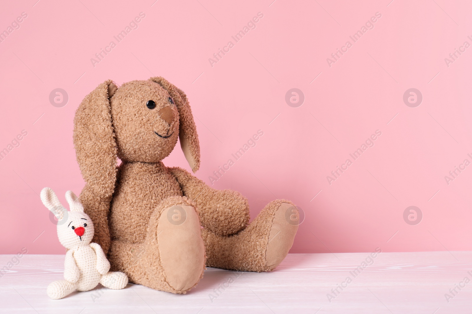 Photo of Adorable toy bunnies on table against color background, space for text. Child room elements