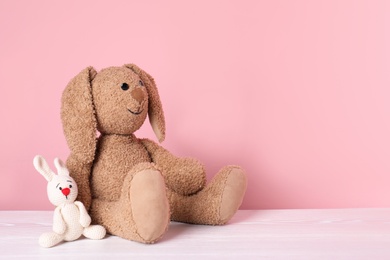 Adorable toy bunnies on table against color background, space for text. Child room elements