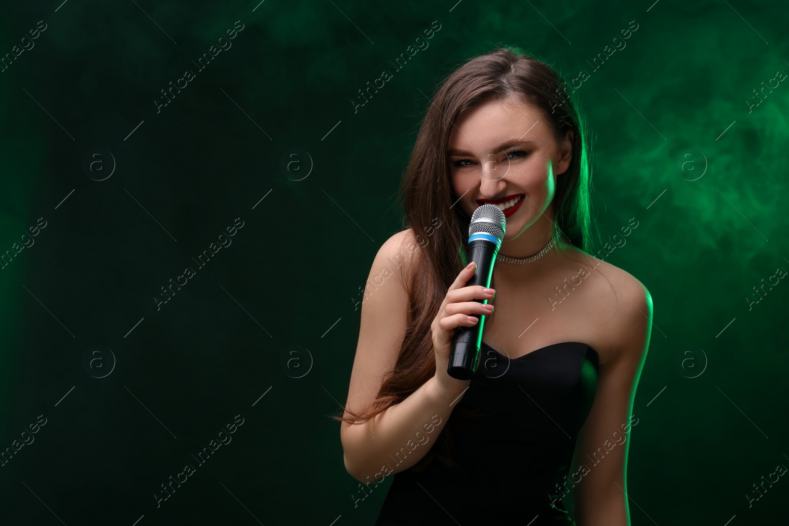 Photo of Beautiful woman with microphone singing in color lights on dark background. Space for text