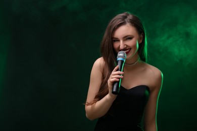 Photo of Beautiful woman with microphone singing in color lights on dark background. Space for text