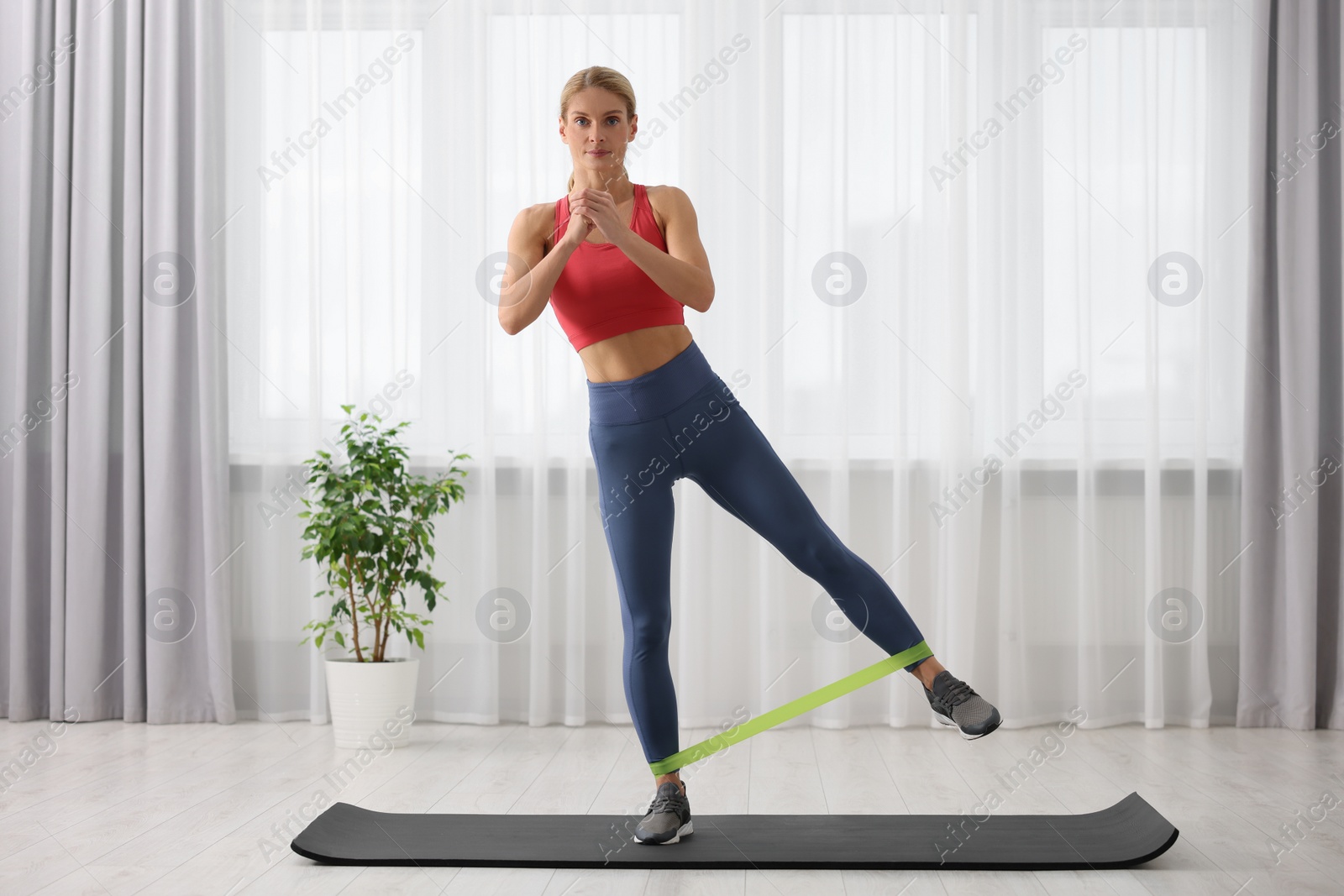 Photo of Athletic woman doing exercise with fitness elastic band on mat at home