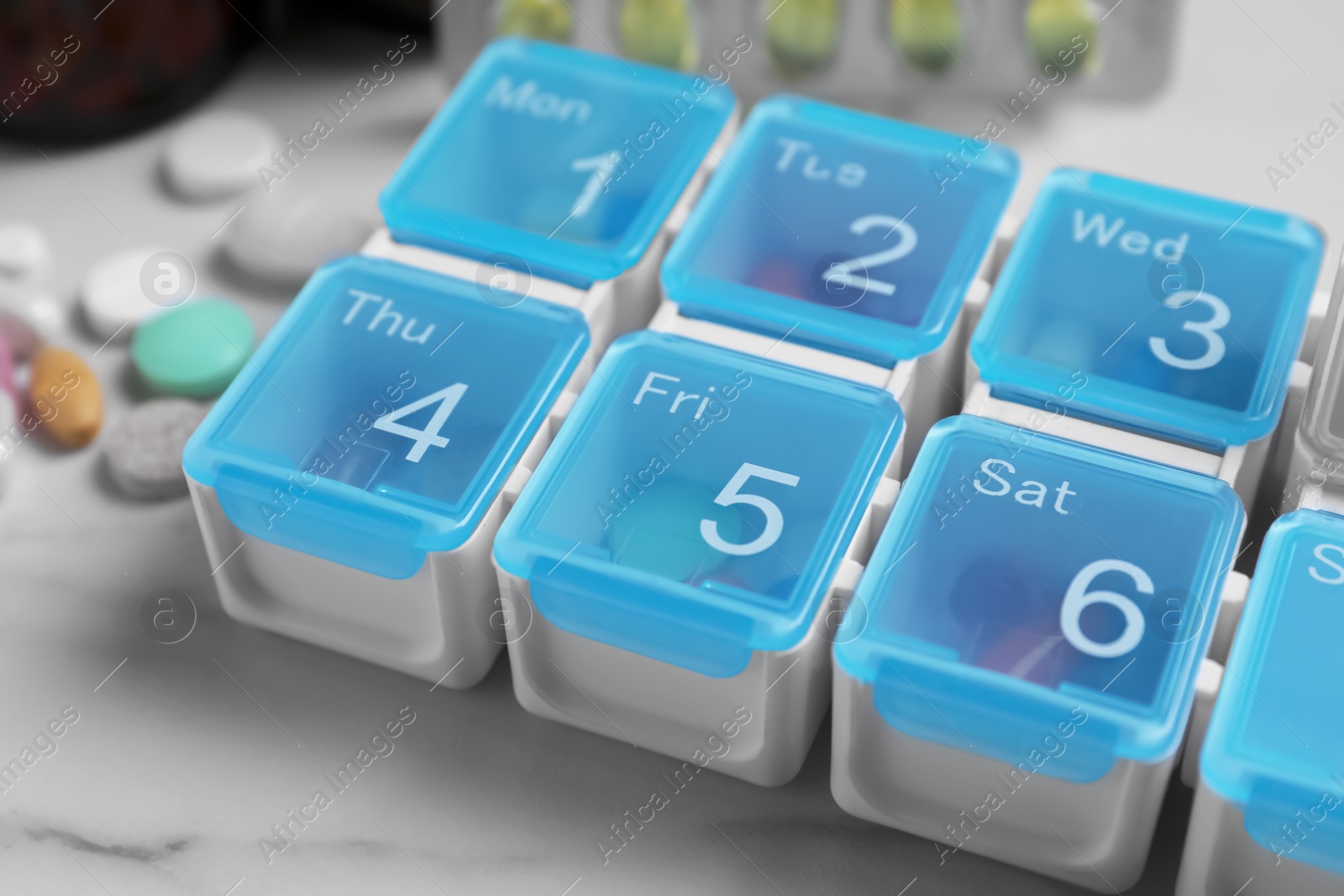 Photo of Weekly pill box with medicaments on white marble table, closeup