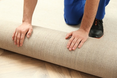 Photo of Worker rolling out new carpet flooring indoors, closeup