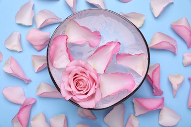 Photo of Bowl with water and rose petals on light blue background, flat lay. Spa composition