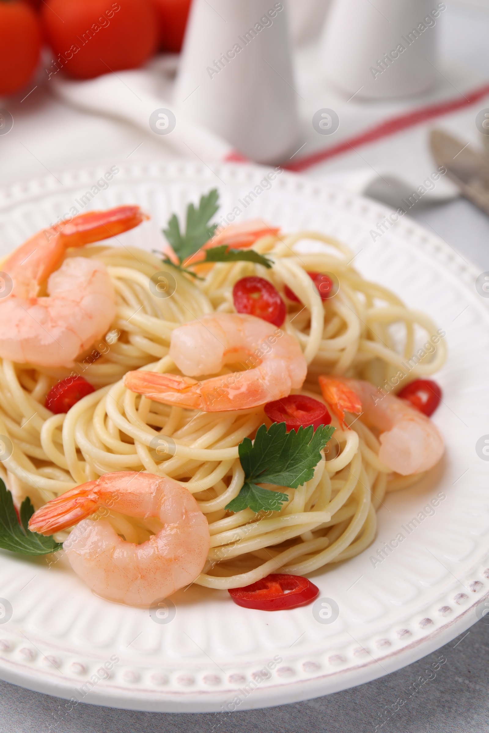 Photo of Tasty spaghetti with shrimps, chili pepper and parsley on grey table, closeup