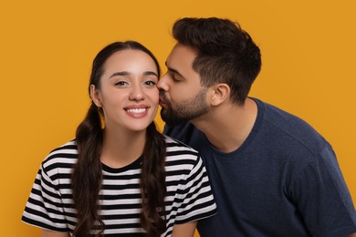 Man kissing his smiling girlfriend on orange background