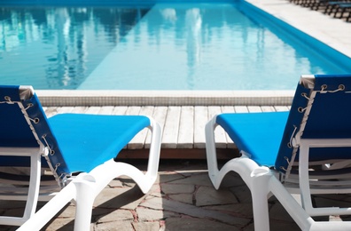 Comfortable loungers at clean swimming pool on sunny day