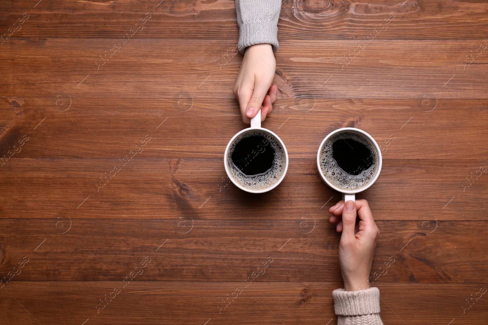 Photo of Women with cups of coffee at wooden table, top view. Space for text