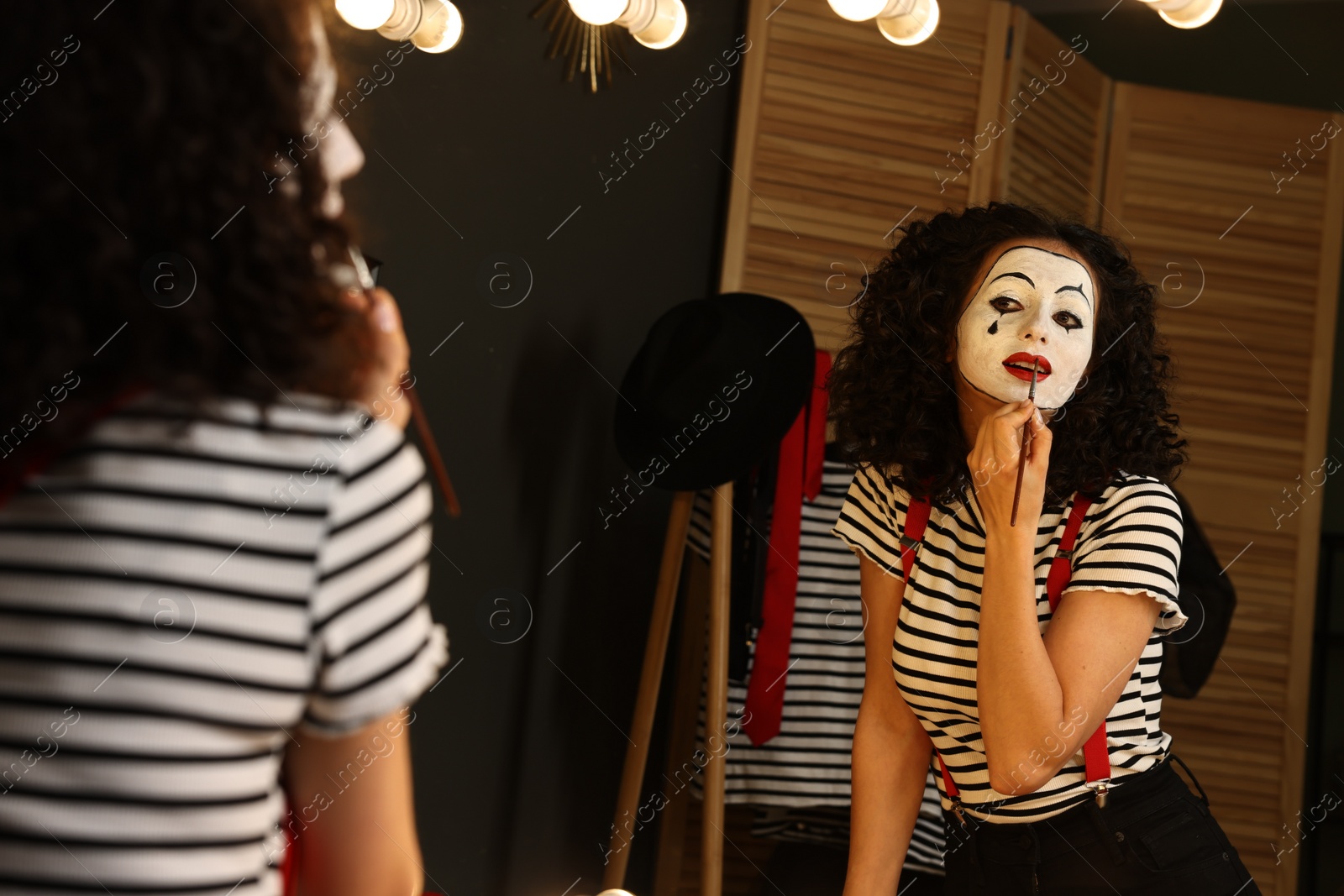 Photo of Young woman applying mime makeup near mirror indoors