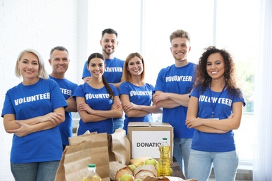 Team of volunteers near table with food donations indoors