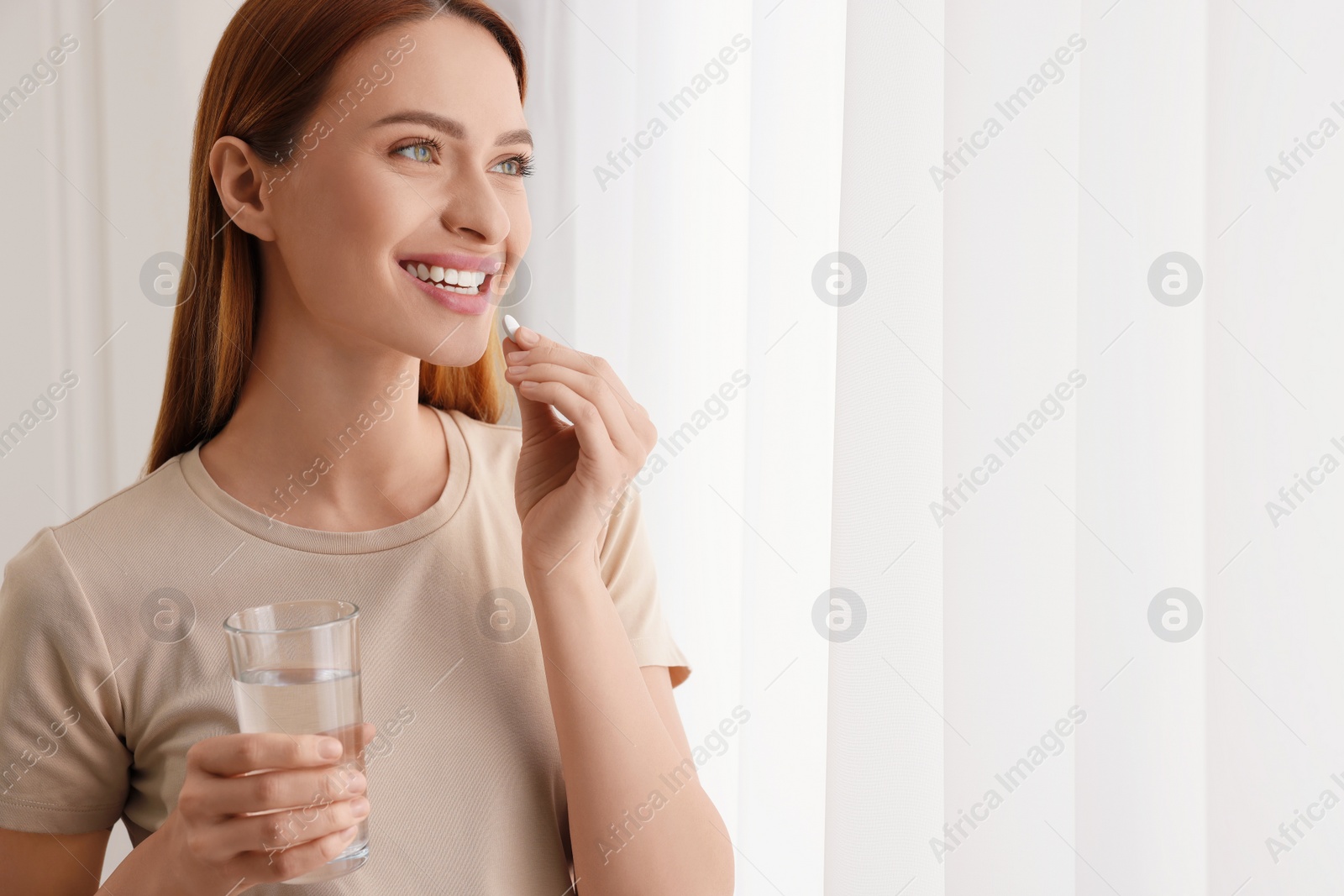 Photo of Beautiful young woman taking vitamin pill at home. Space for text