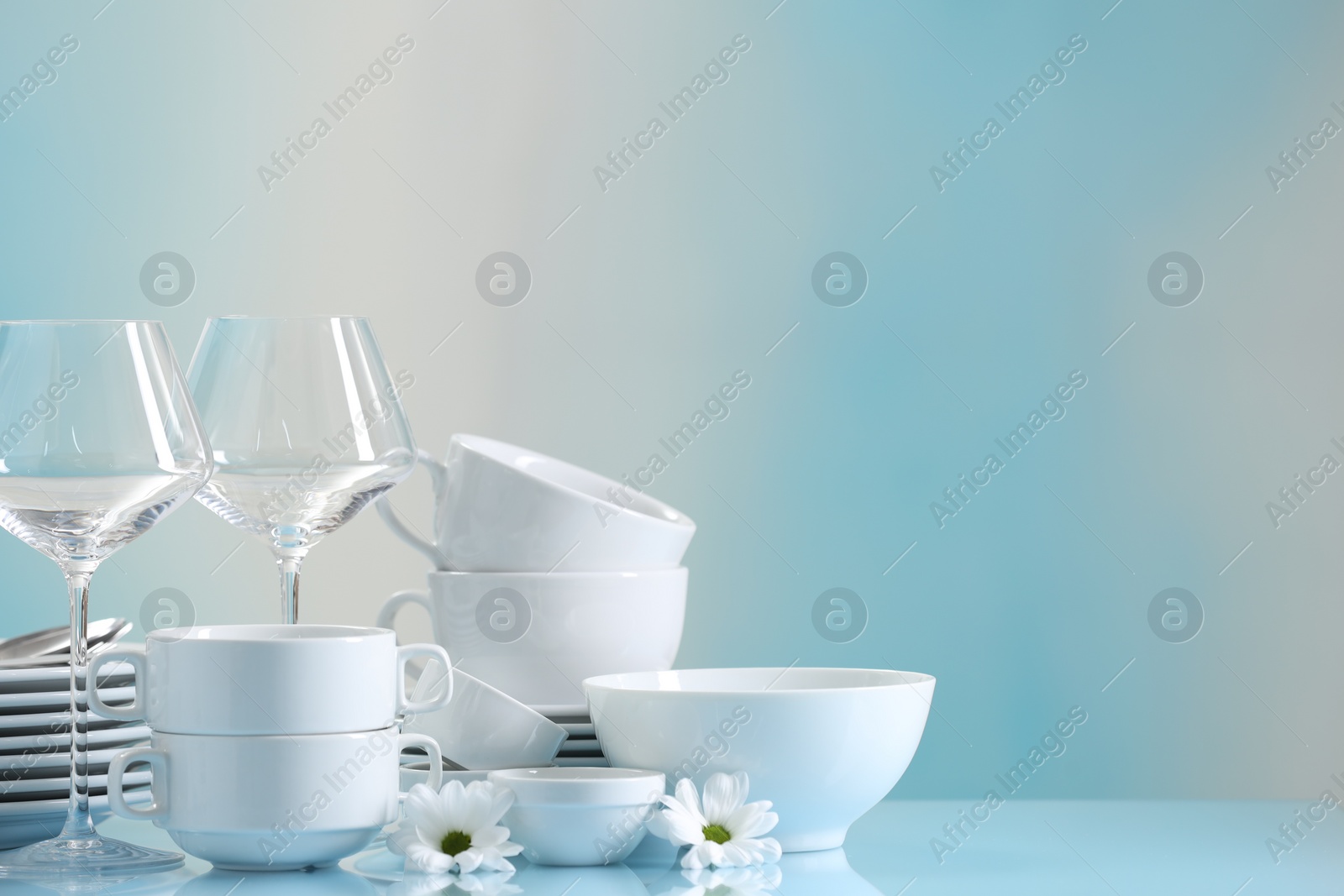 Photo of Set of many clean dishware, flowers and glasses on light blue table. Space for text