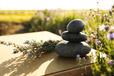 Photo of Stack of spa stones on wooden table in lavender field. Harmony and zen