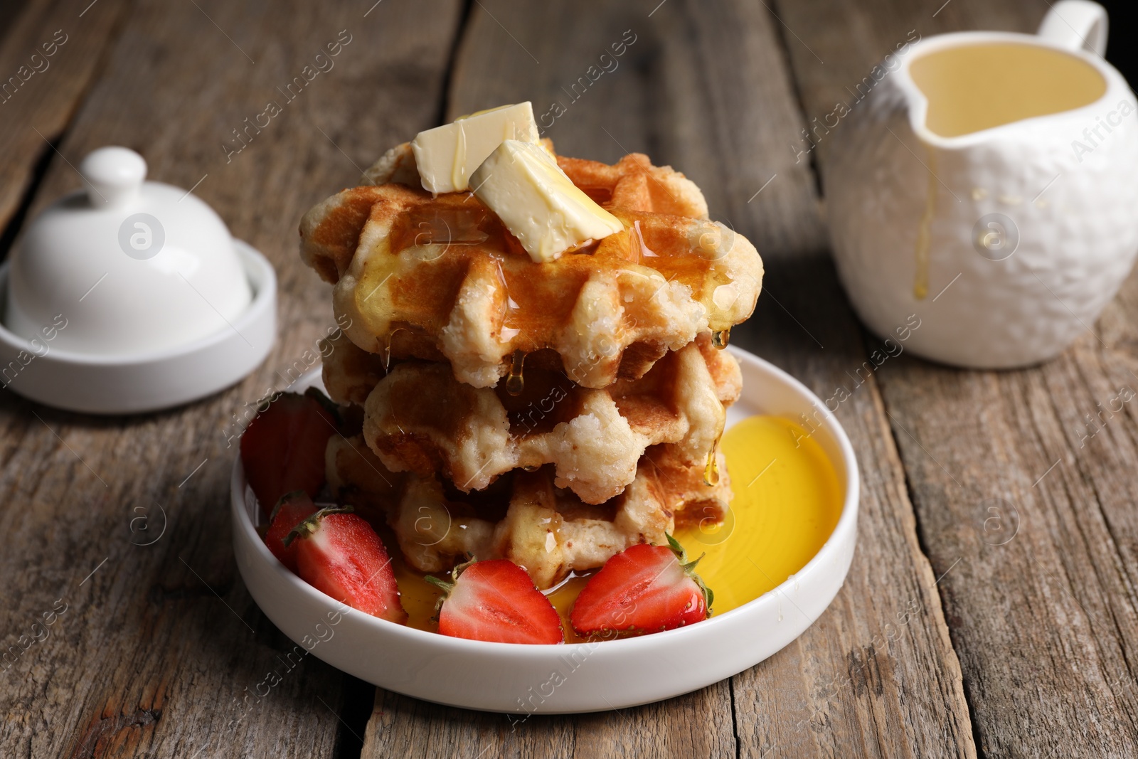 Photo of Delicious Belgian waffles with honey, butter and strawberries on wooden table