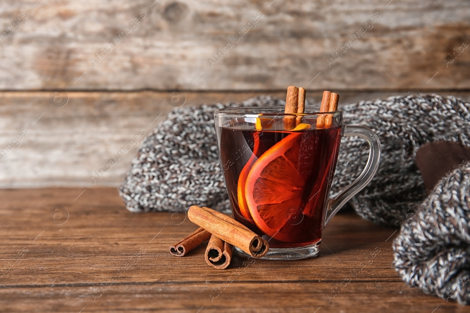 Photo of Cup with red mulled wine on table against wooden background