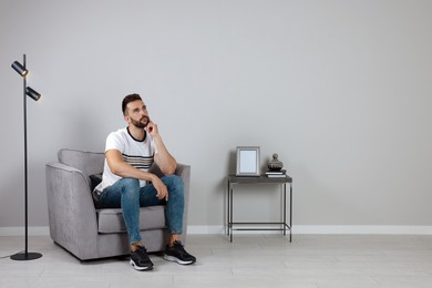 Photo of Man sitting in armchair near gray wall, space for text