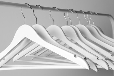 White clothes hangers on metal rail against light background, closeup