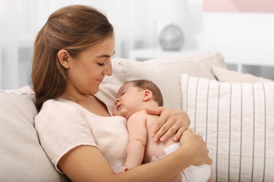 Mother holding her cute newborn baby on sofa indoors, space for text