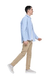 Photo of Young man in light blue shirt and beige pants walking on white background