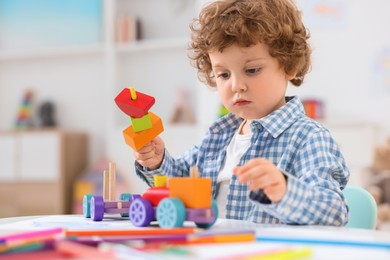 Photo of Cute little boy playing with wooden toys at white table in kindergarten