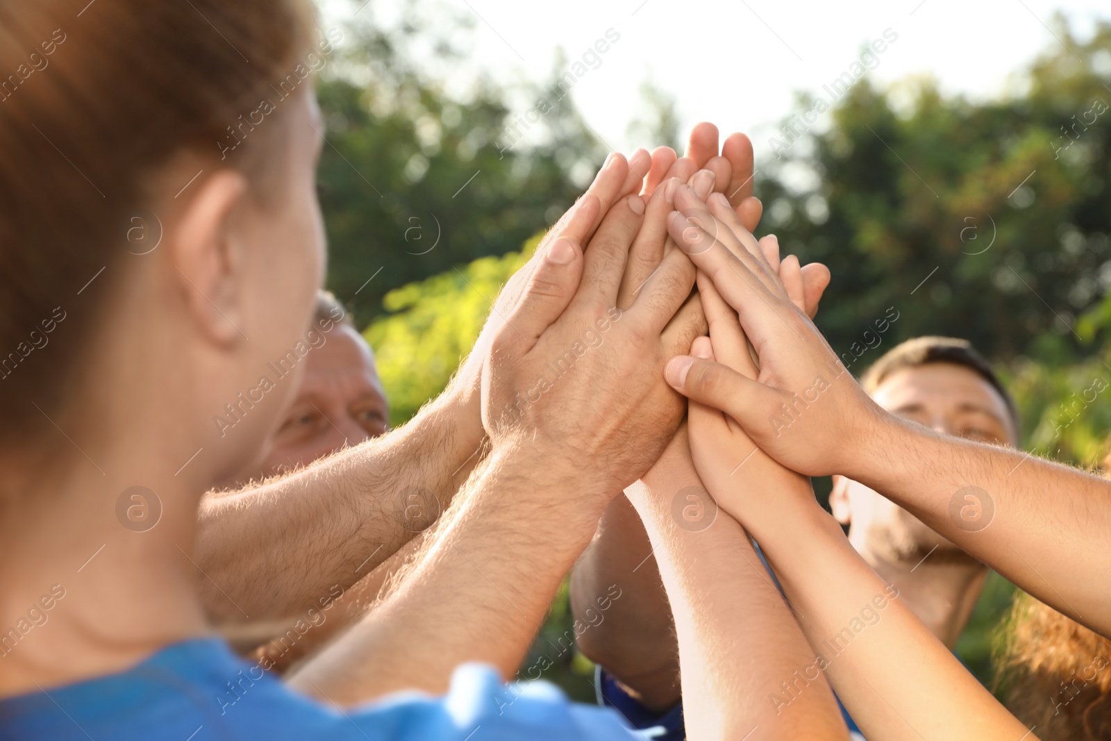 Photo of Group of volunteers joining hands together outdoors on sunny day