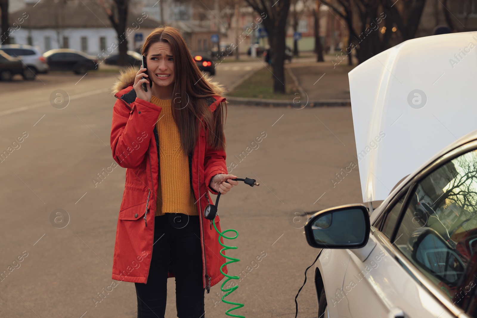 Photo of Young woman having difficulties while inflating car tire on street