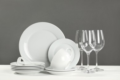 Set of clean dishware and glasses on white wooden table against grey background