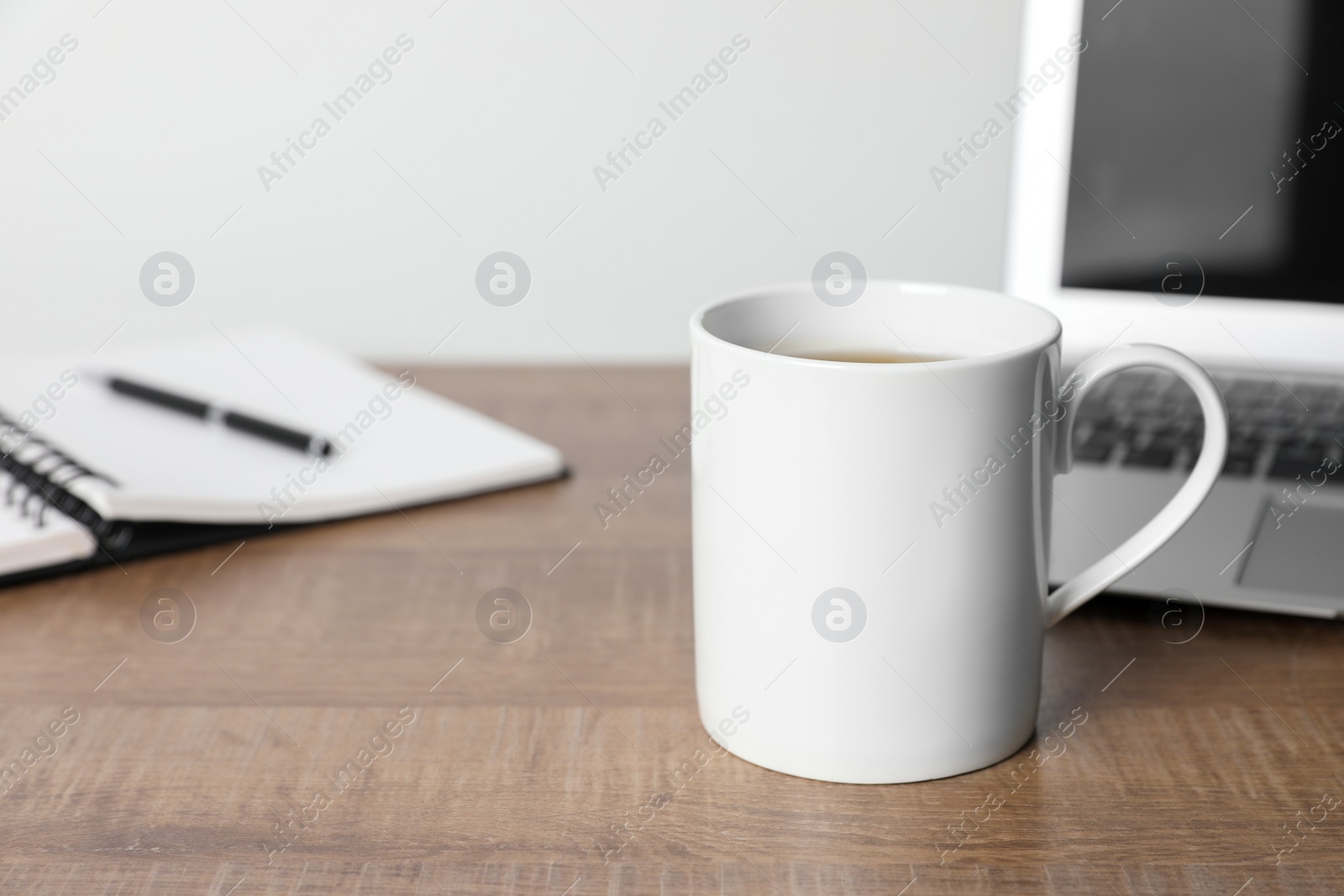 White ceramic mug with drink, notebook and laptop on wooden table at workspace, space for text Photo of White ceramic mug with drink, notebook and laptop on wooden table at workspace, space for text
