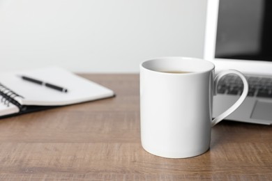 Photo of White ceramic mug with drink, notebook and laptop on wooden table at workspace, space for text