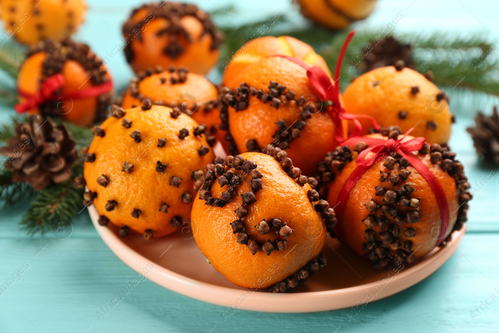 Photo of Pomander balls made of fresh tangerines and cloves on light blue table, closeup