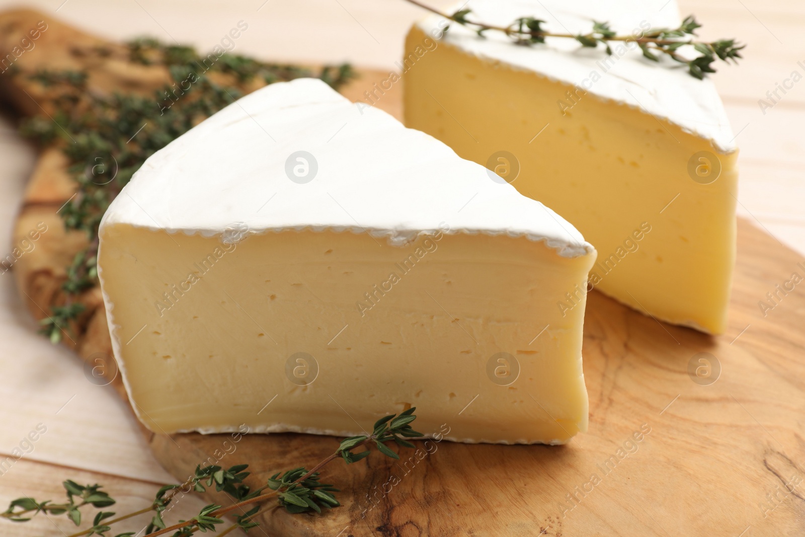 Photo of Board with pieces of tasty camembert cheese and thyme on light wooden table, closeup