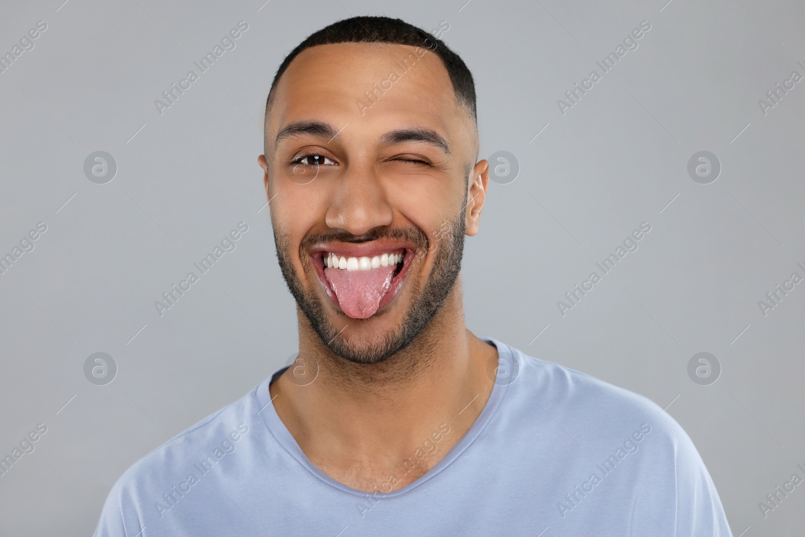 Photo of Happy young man showing his tongue on light grey background