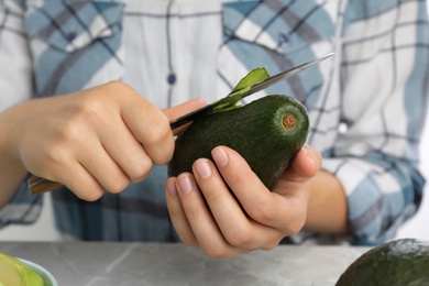 Photo of Woman peeling ripe avocado at table, closeup