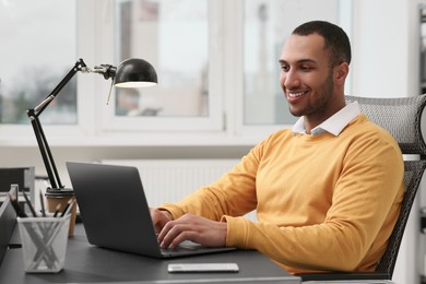 Photo of Young man working on laptop at table in office