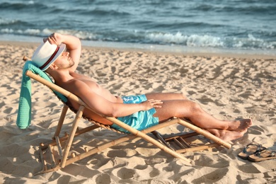 Photo of Young man relaxing in deck chair on beach near sea