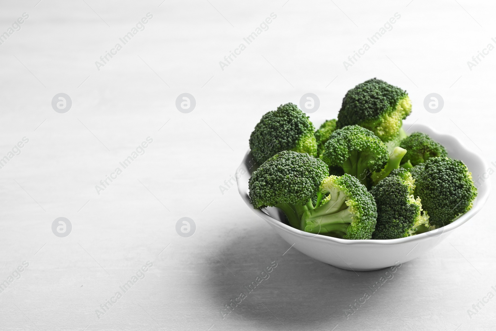 Photo of Bowl of fresh broccoli on light grey table, space for text