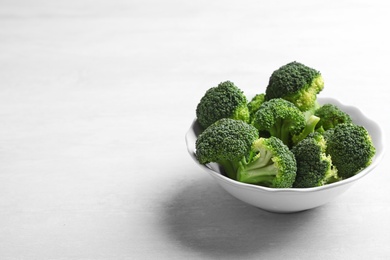 Bowl of fresh broccoli on light grey table, space for text