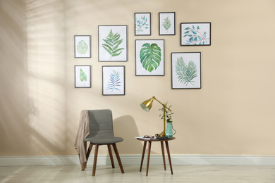 Photo of Beautiful paintings of tropical leaves on beige wall in room interior
