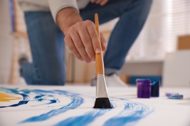 Photo of Young man painting on canvas with brush in artist studio, closeup
