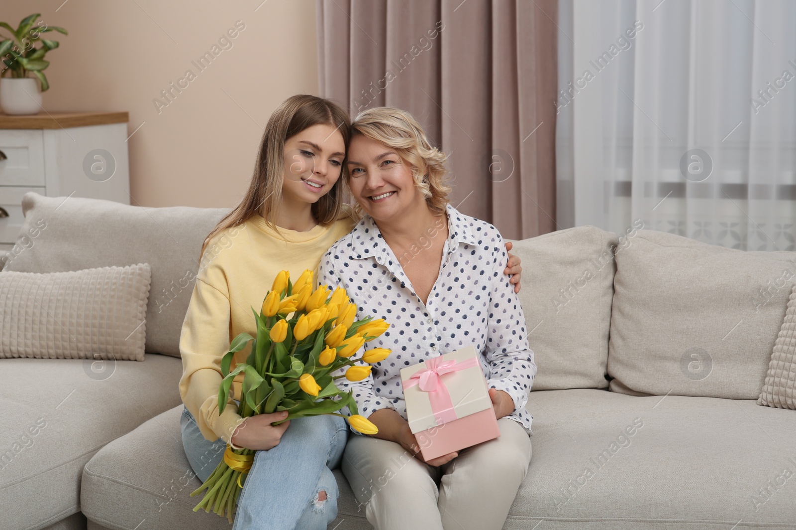 Photo of Young daughter congratulating her mom with flowers and gift at home. Happy Mother's Day