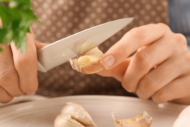 Photo of Woman peeling fresh garlic at table, closeup