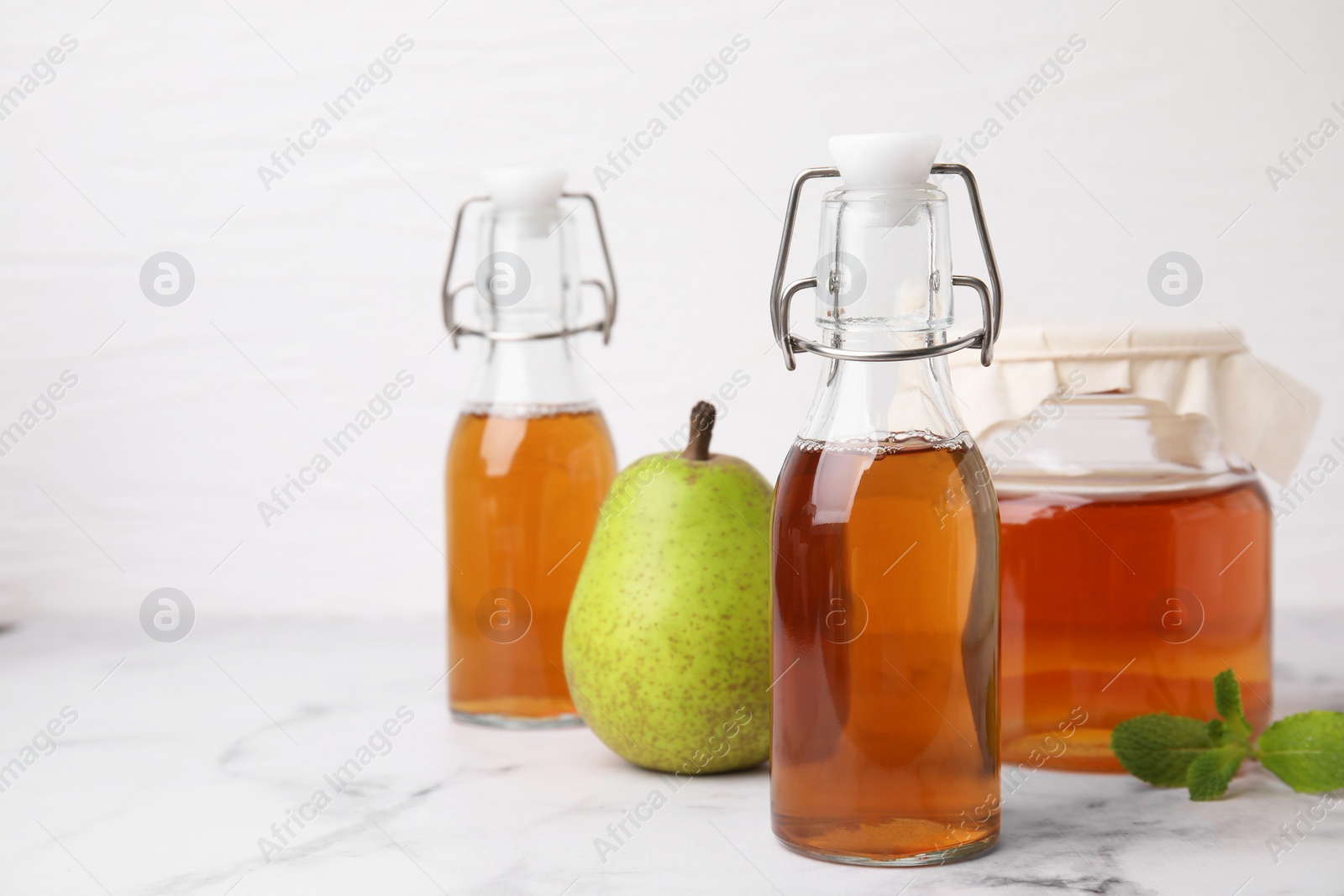 Photo of Tasty kombucha, pear and mint on white marble table, space for text