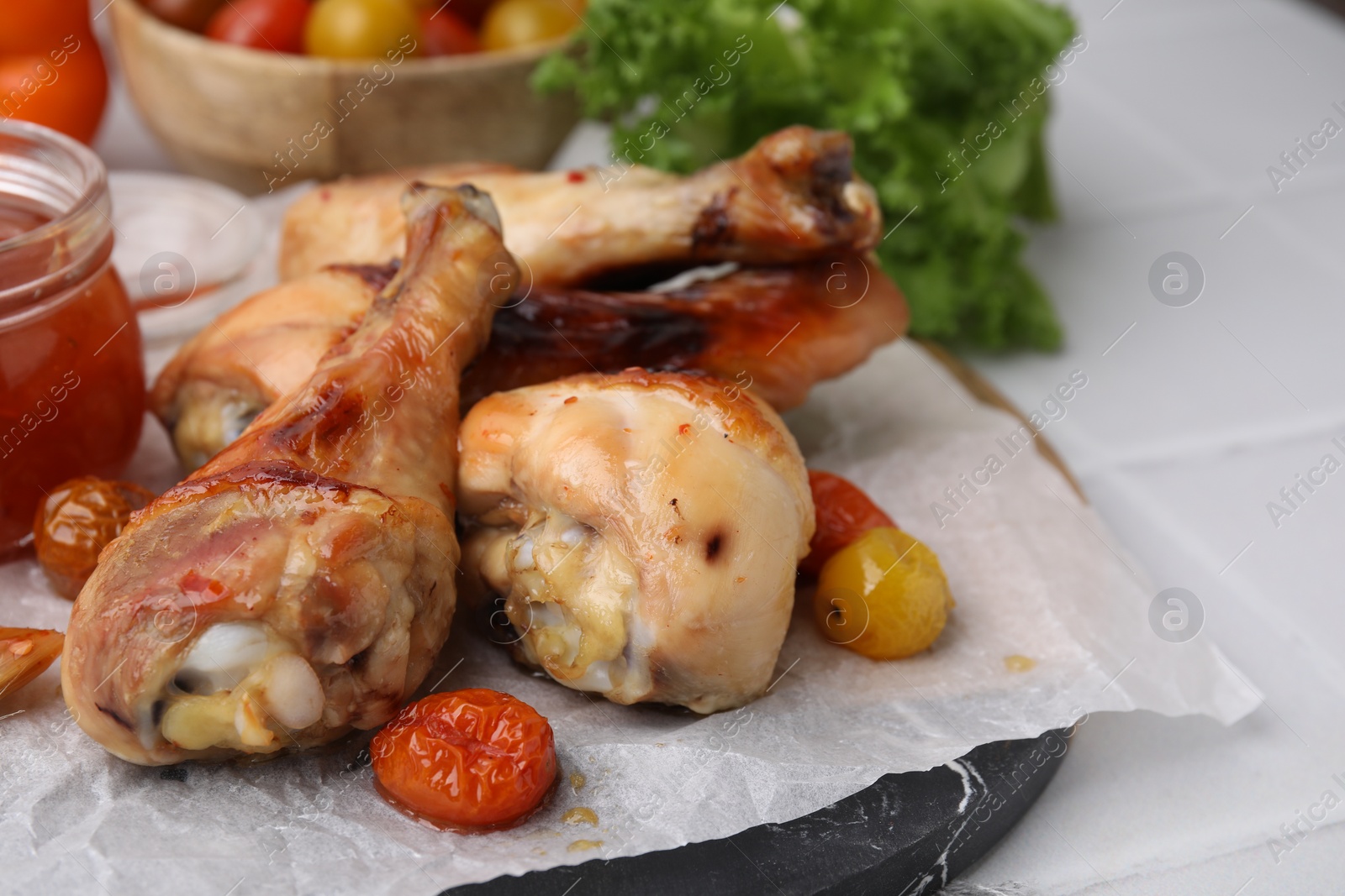 Photo of Roasted chicken drumsticks, tomatoes and marinade on white tiled table, closeup