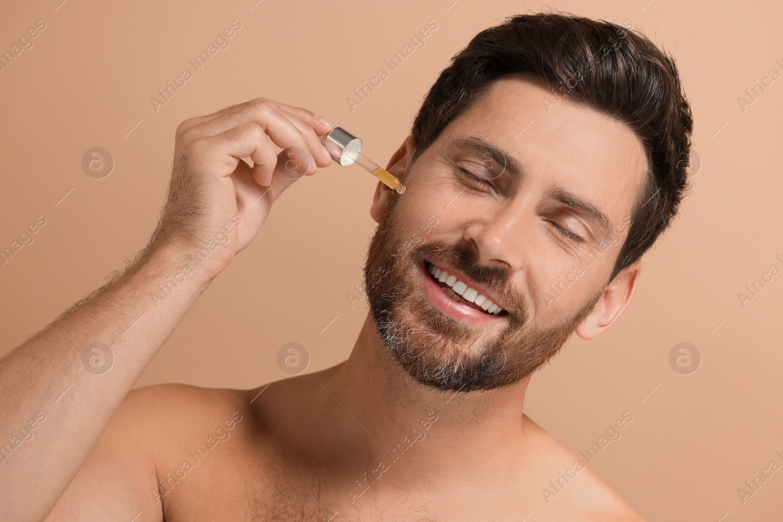 Photo of Smiling man applying cosmetic serum onto his face on beige background