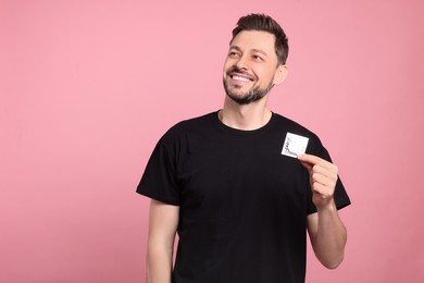 Happy man holding condom on pink background. Space for text